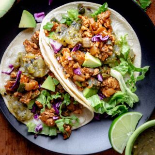 a black plate with two ground chicken tacos on it