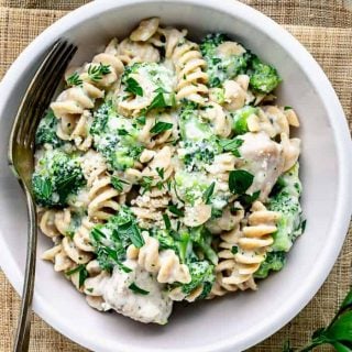 A close up of a pale pink bowl with spiral pasta and chicken alfredo with broccoli