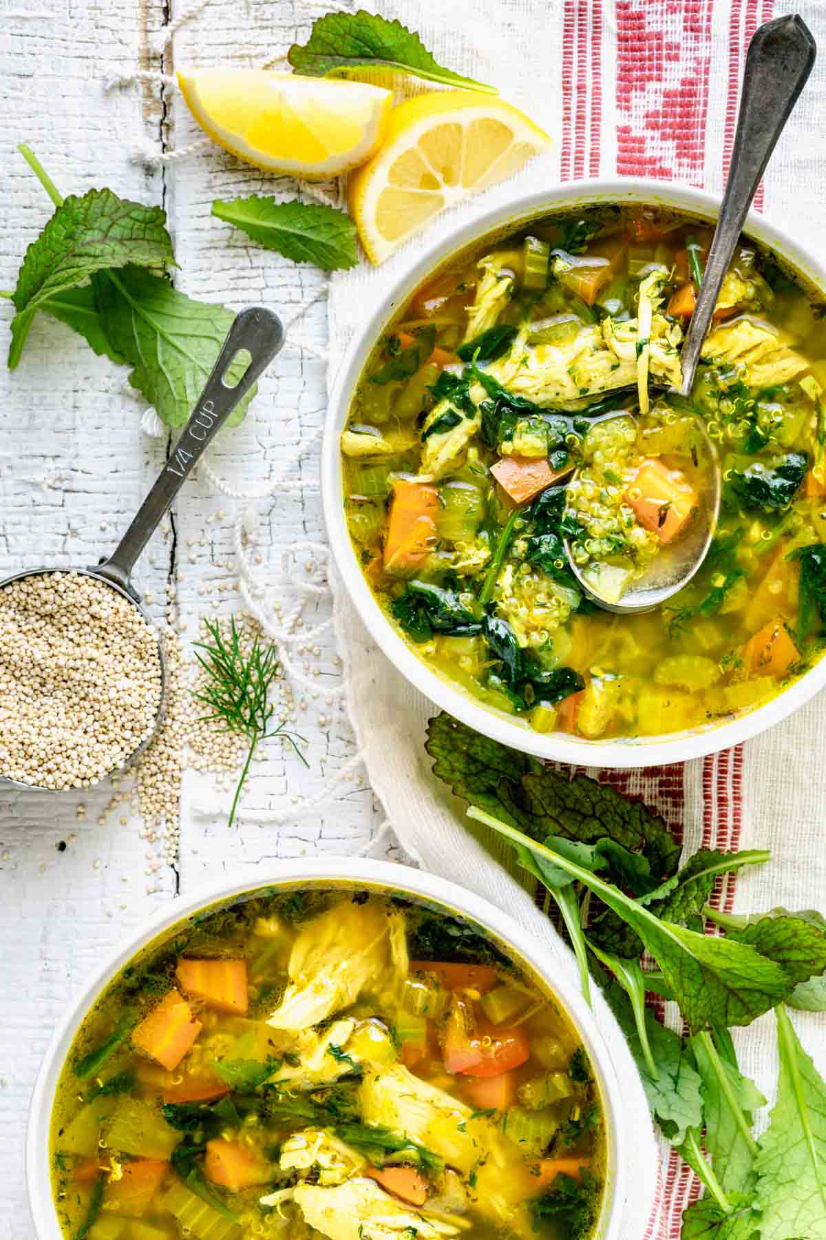 chicken quinoa soup in two bowls with a measuring cup of quinoa on the table next to them