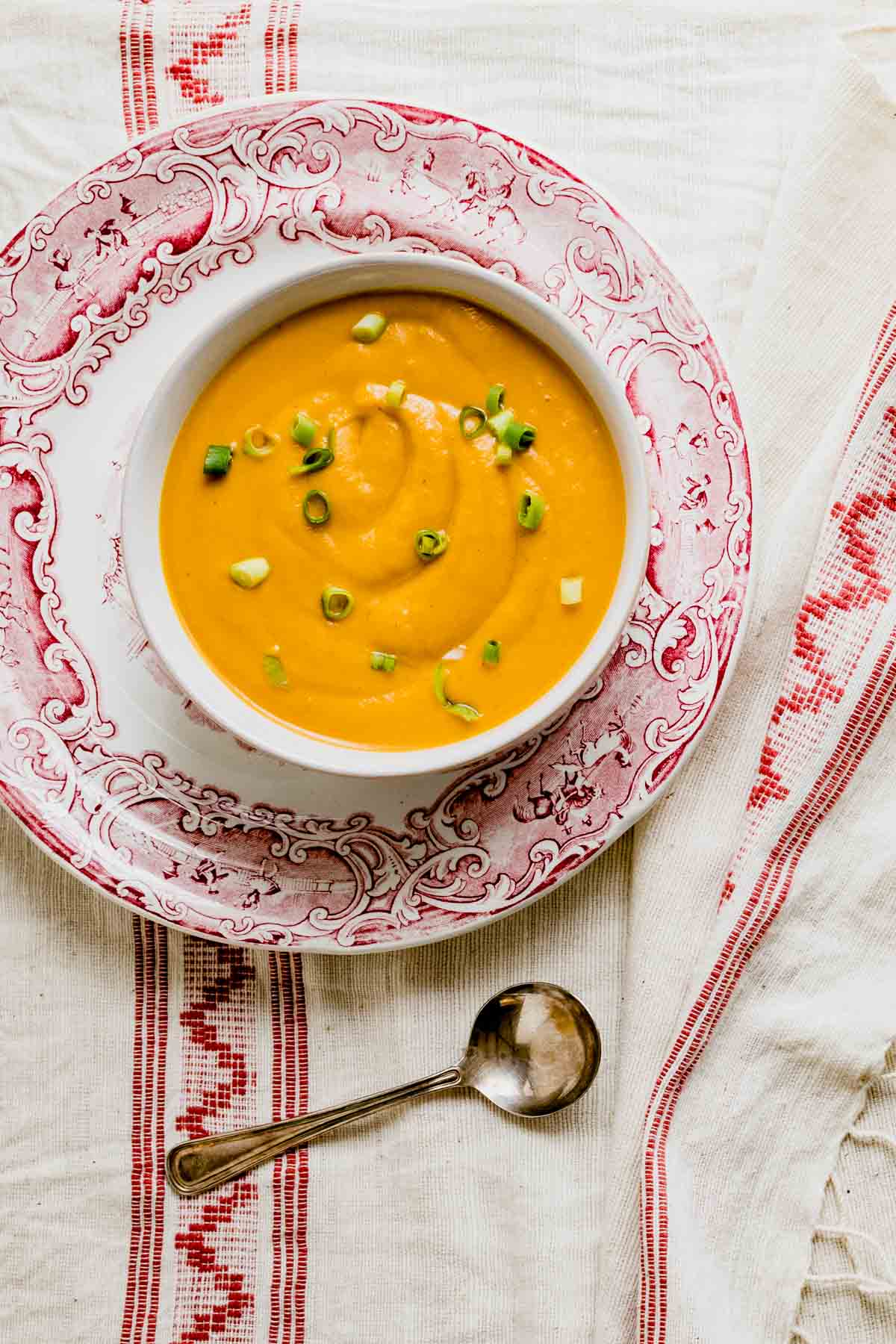 a bowl of soup on a plate with red rim and a red napkin underneath