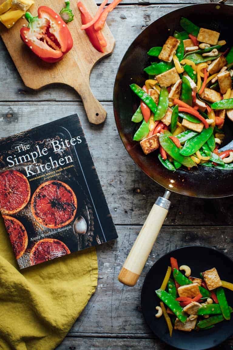 veggie stir fry in a wok next to a cookbook