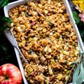 a white casserole dish filled with stuffing with apples around it