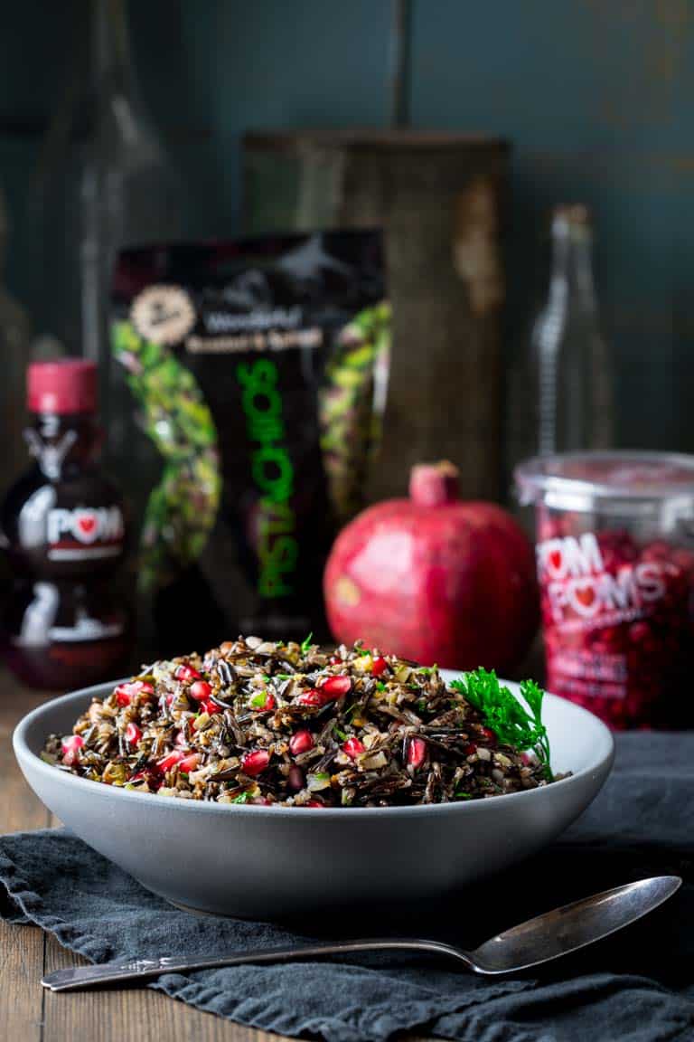 A side shot of a bowl full of wild rice pilaf salad, with a whole pomegranate alongside.