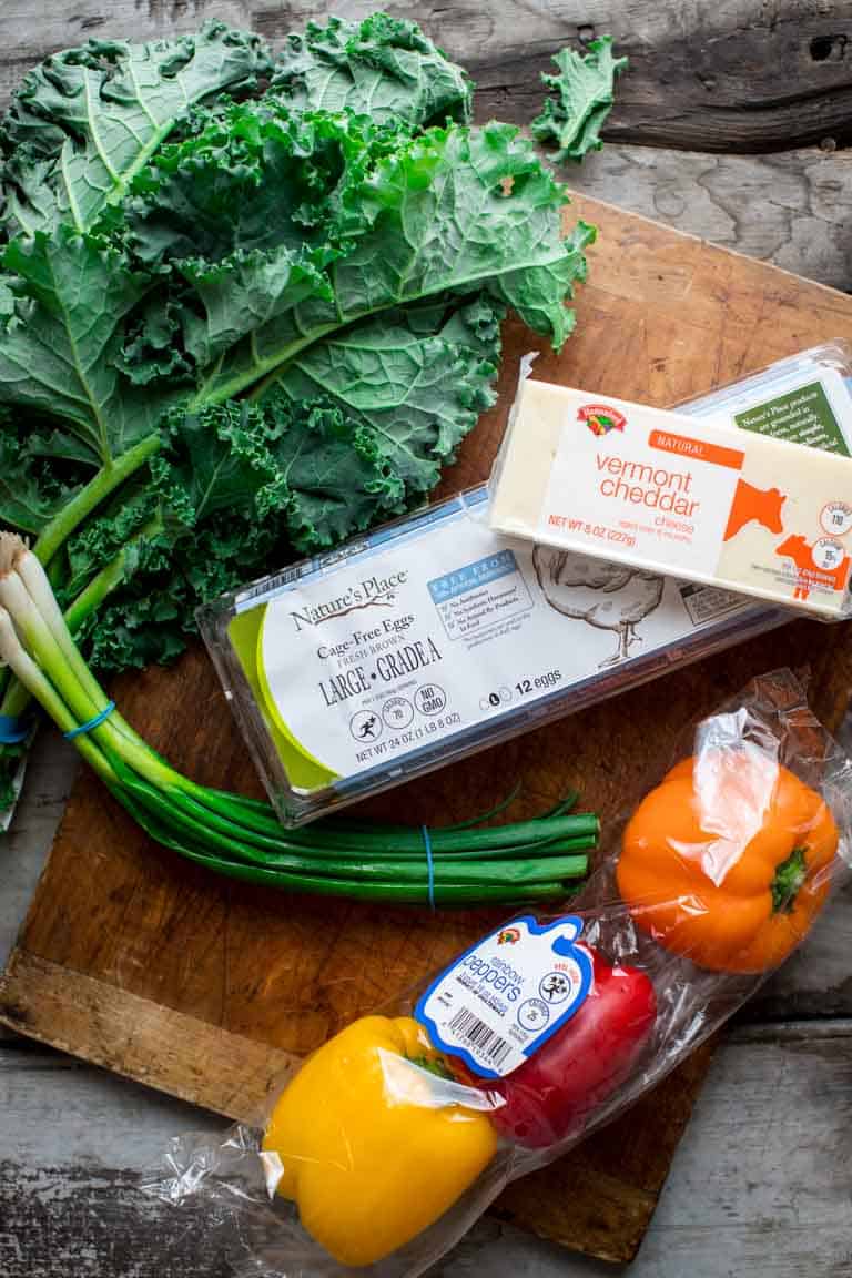 eggs, cheddar, veggies and kale placed on a cutting board