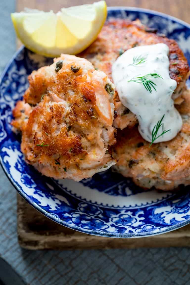A blue and white dish with a few salmon cakes on it. They have a dollop of greek yogurt hollandaise on them and a sprinkle of dill