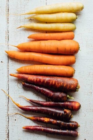 all different colored carrots lined up on a white surface