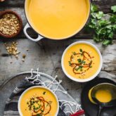 a pot with soup and two bowls from overhead with garnishes on a rustic gray tabletop