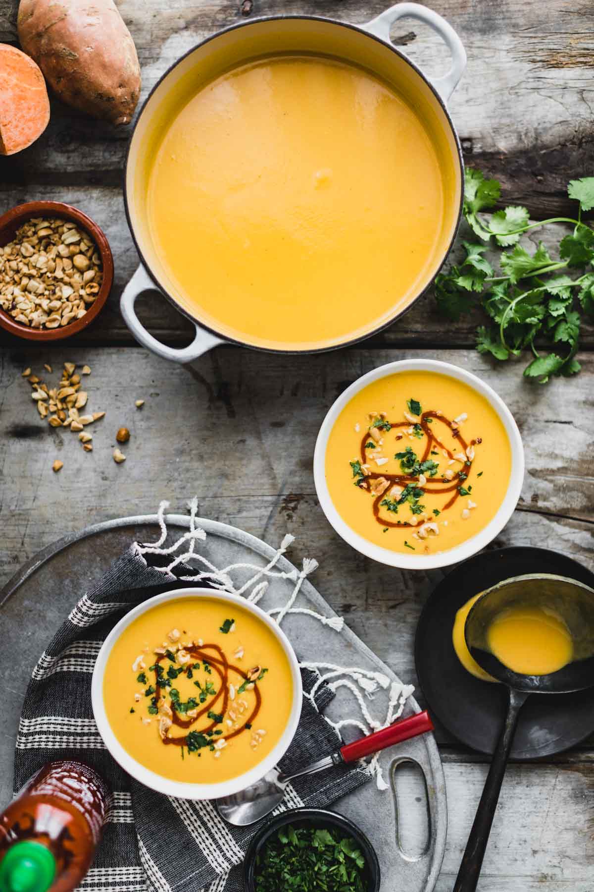 a pot with soup and two bowls from overhead with garnishes on a rustic gray tabletop