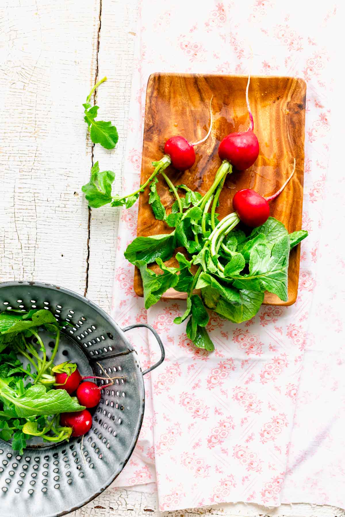 the radishes on a table with a wooden plate and colander