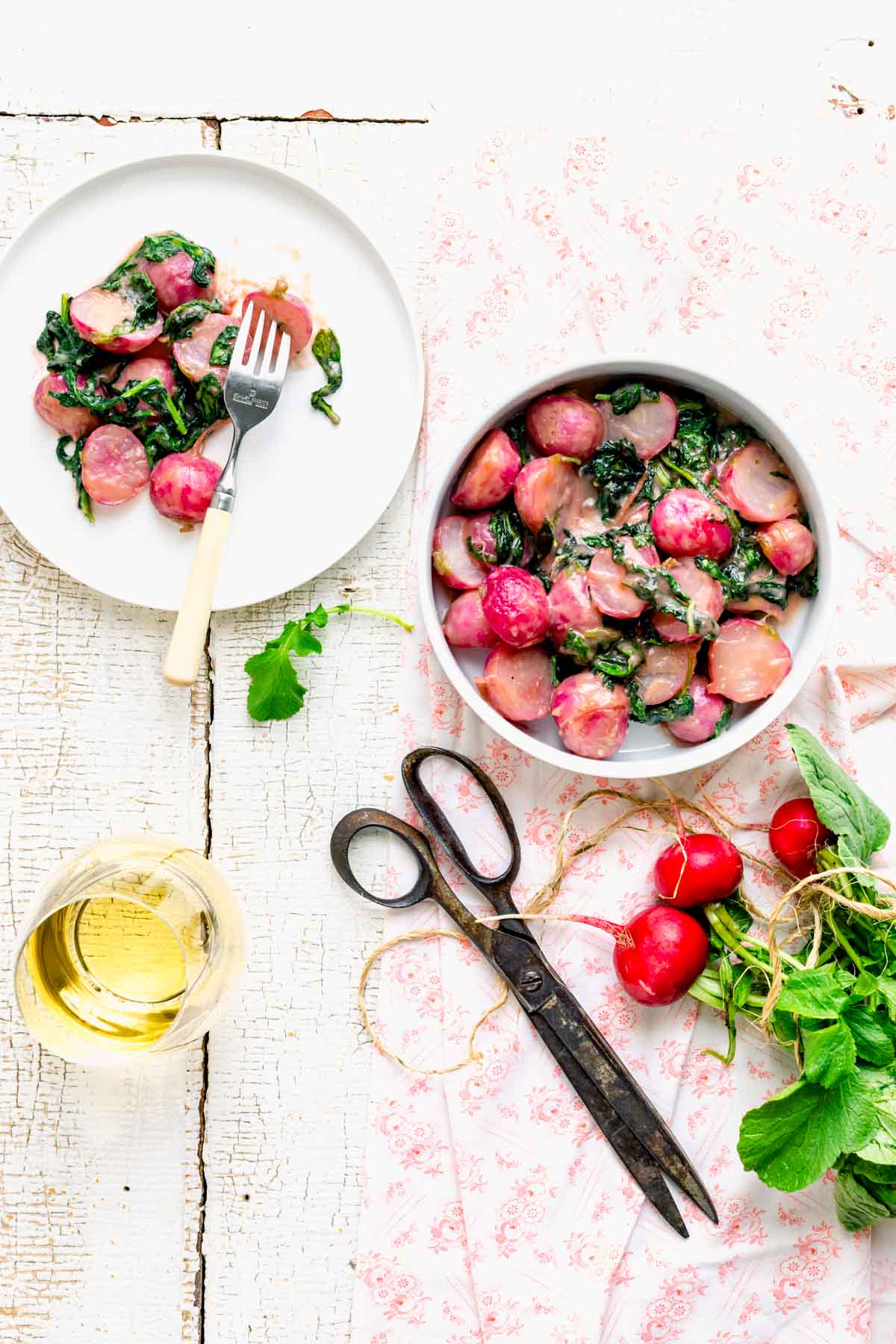 a tablescape with the recipe a bunch of radishes, scissors and a glass of white wine