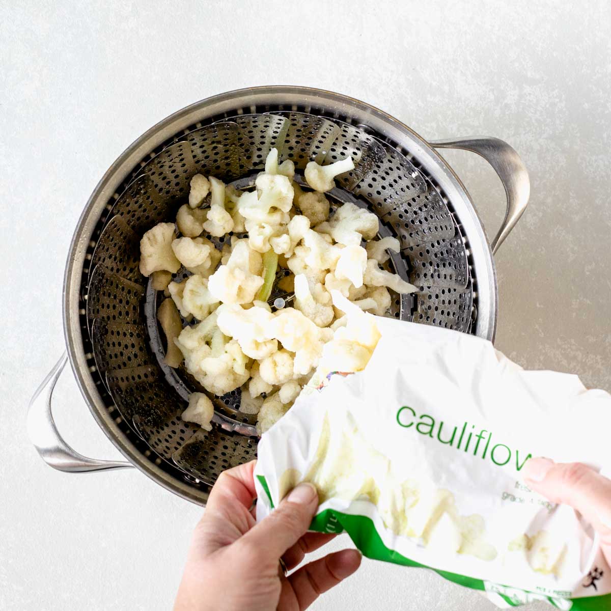 adding frozen cauliflower to the steamer basket