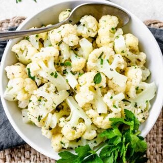 white bowl with herbed cauliflower with sprigs of parsley and a spoon resting in the bowl