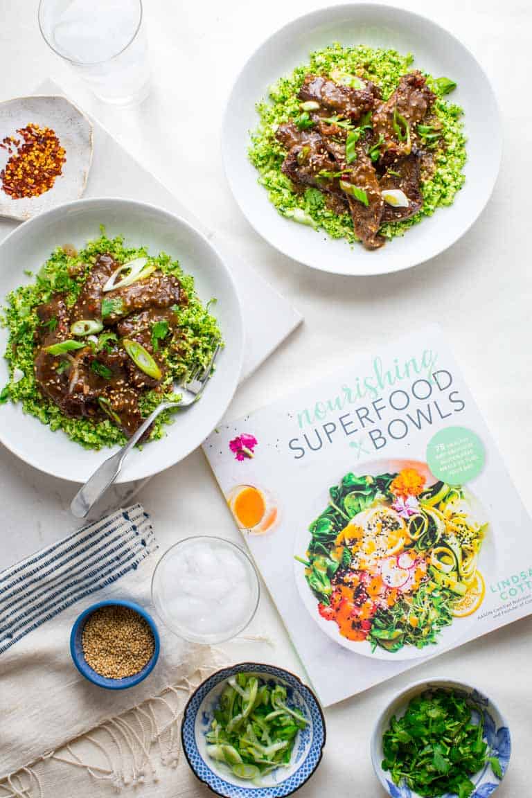 a couple bowls of mongolian beef and broccoli beside the book nourishing superfood bowls
