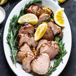 a platter of pork tenderloin with rosemary sprigs and slices of lemon