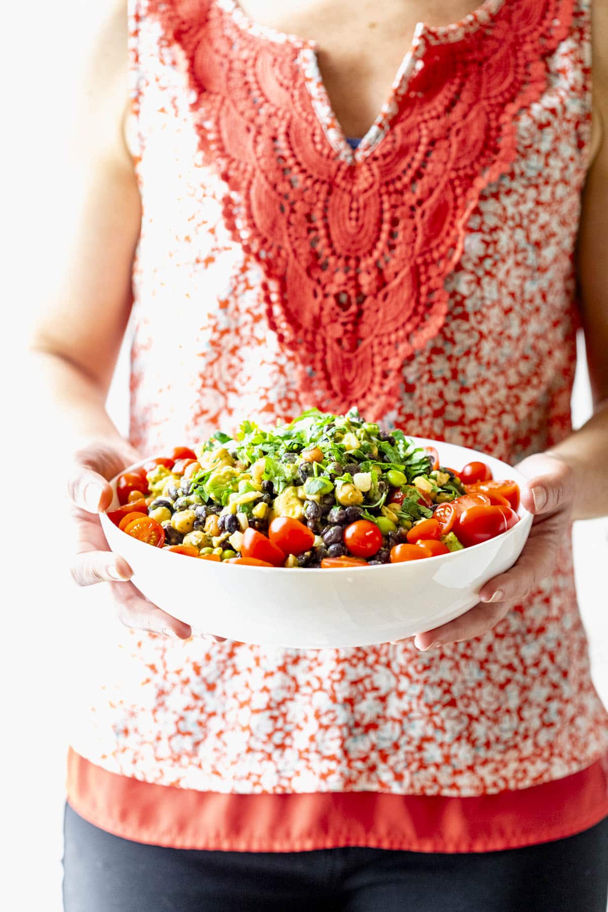 a woman in a red blouse holding the bowl of bean salad