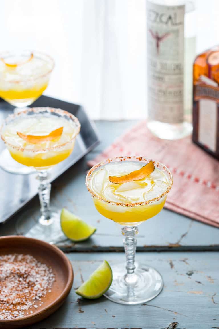 These smoky, tart and sweet Mescal Margaritas, made with Cuantro, freshly squeezed lime and orange juice have a salted rim with a surprising ingredient! #mescal #margarita #cocktail #cincodemayo #vegan #lime #mexican