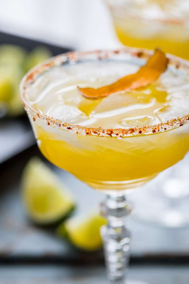 Close up of a Smoky Mezcal Margarita with a salted rim and lime slices and another margarita in the background