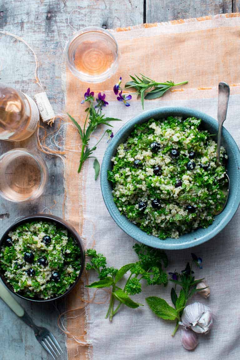 two bowls of blueberry quinoa tabbouleh on a peach and white cloth with edible flowers