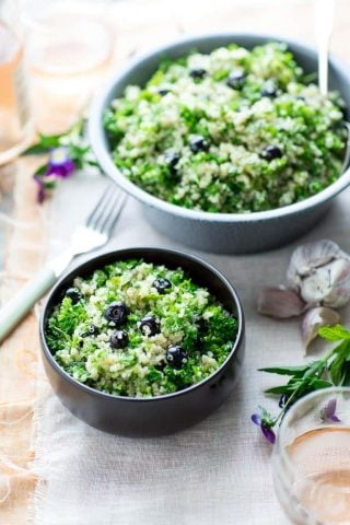 two bowls of blueberry quinoa tabbouleh on a peach and white cloth with edible flowers