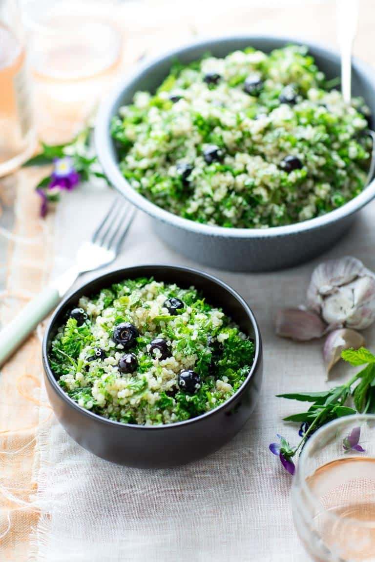 two bowls of blueberry quinoa tabbouleh on a peach and white cloth with edible flowers