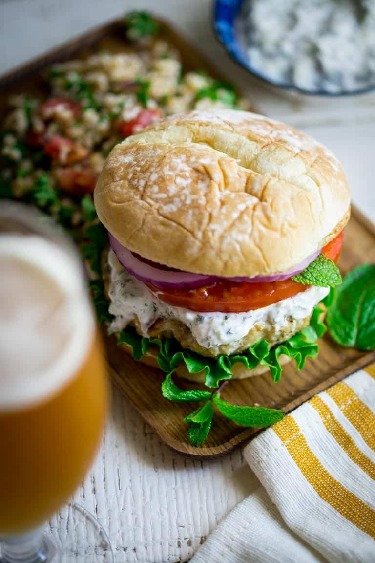 Burgers made from ground chicken, seasoned with za’atar and topped with cucumber mint tzatziki, lettuce and tomato! Get those grills fired up my friends! They’re a middle-eastern flavored burger mash-up you won’t want to miss. Healthy Seasonal Recipes by Katie Webster | #burger #tzatziki #chicken #cucumber #mint #zaatar #grill