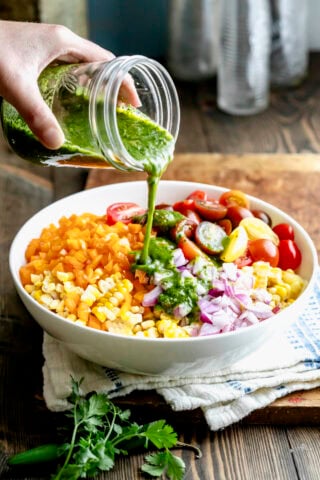a bowl of the ingredients for the corn salad with someone pouring the green dressing on top
