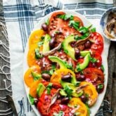 a table scape with rose, a platter of tomato salad and a blue and white cloth