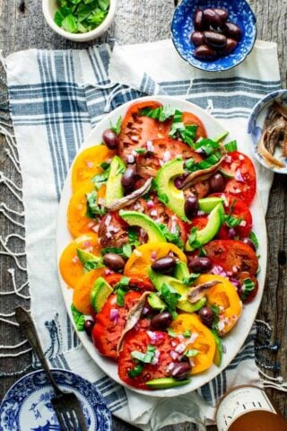 a table scape with rose, a platter of tomato salad and a blue and white cloth