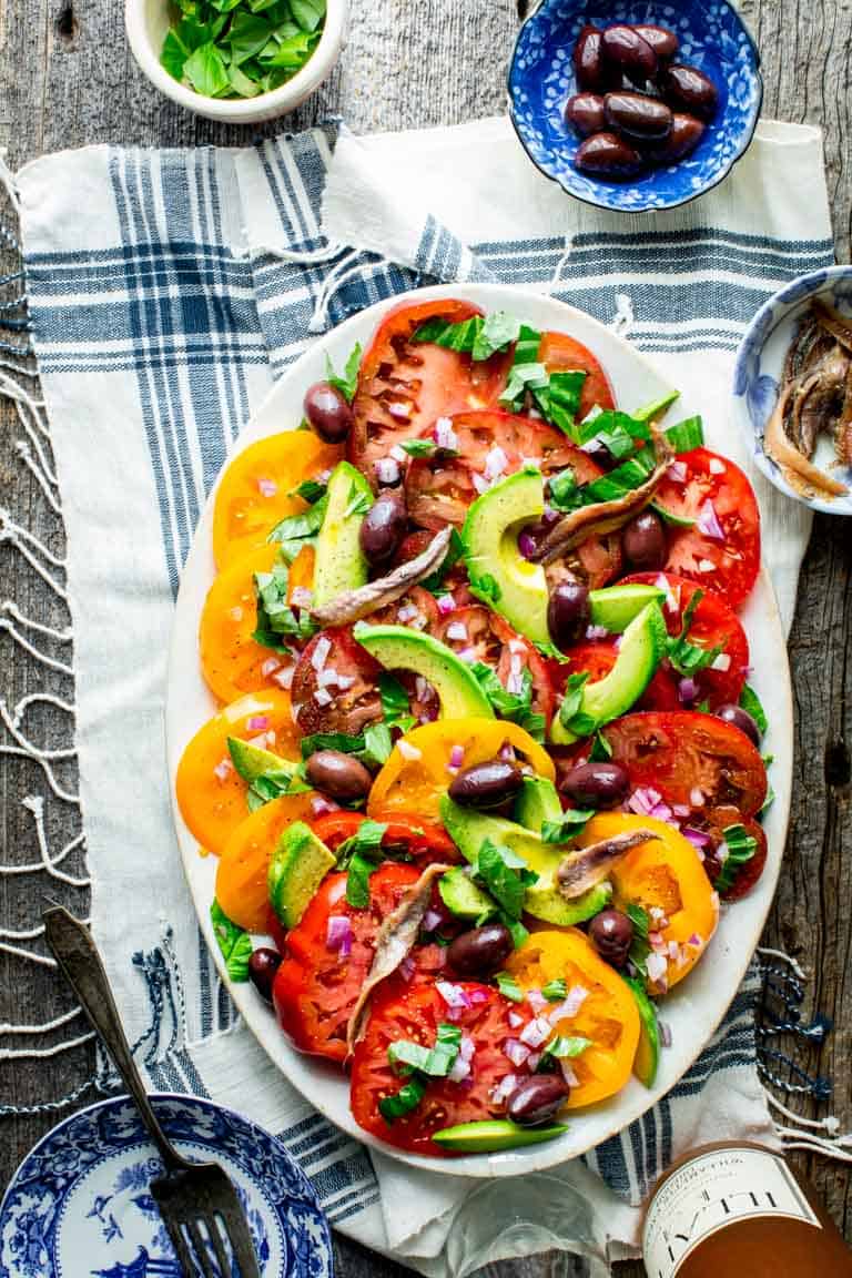 a table scape with rose, a platter of tomato salad and a blue and white cloth