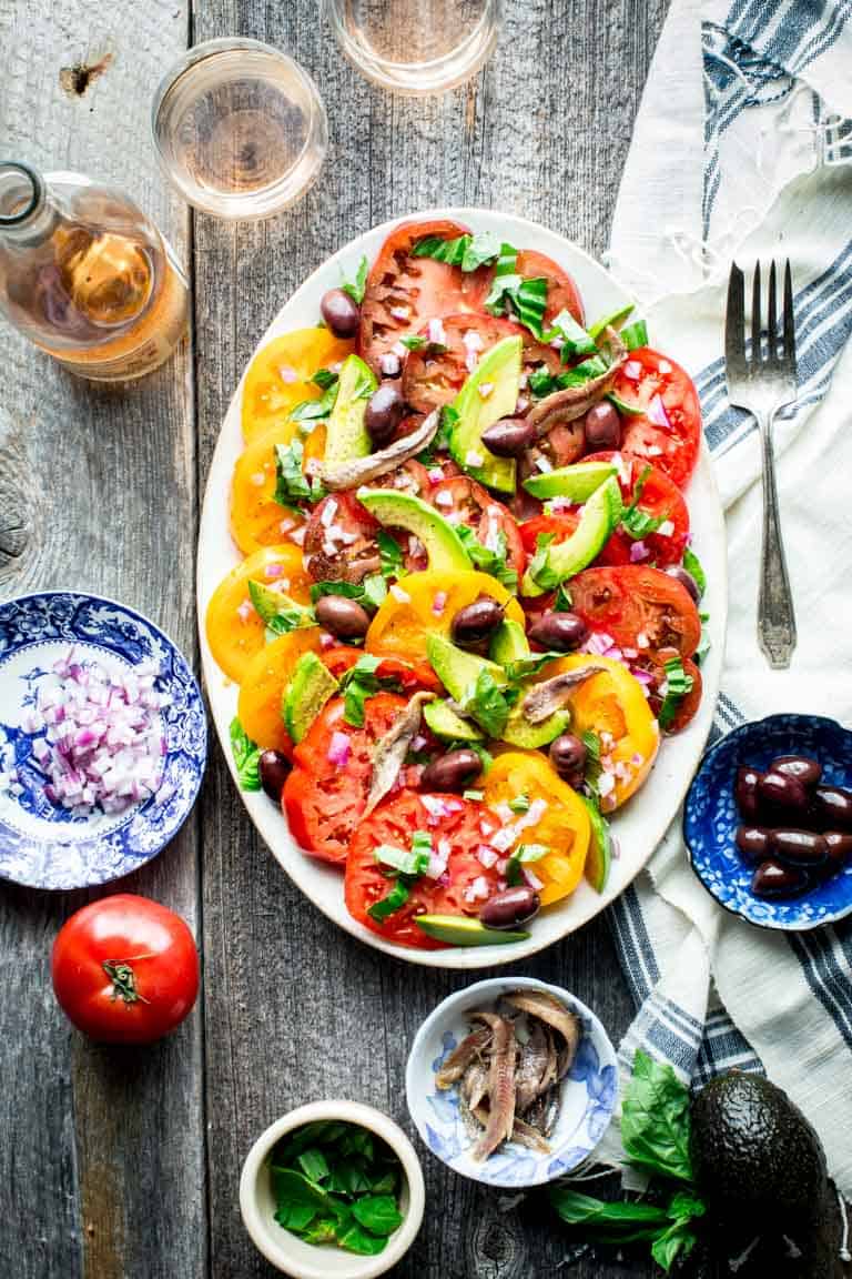 a gray farm table with a platter of tomato salad on it from overhead