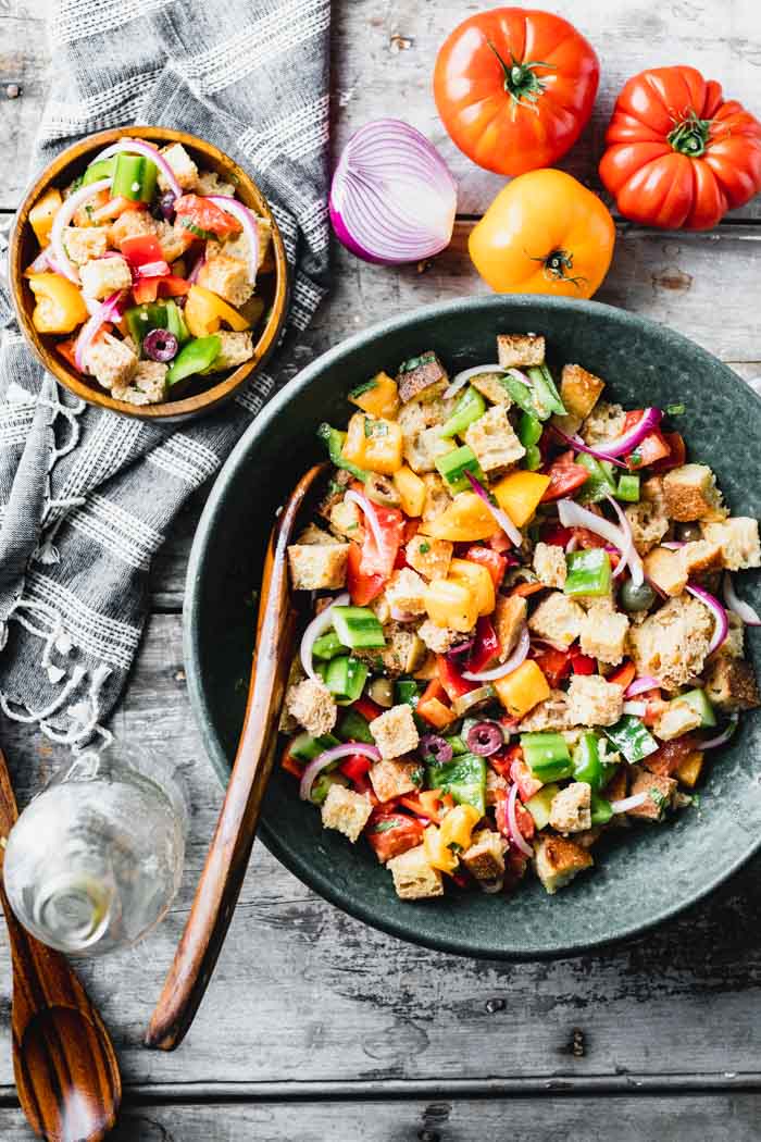 OVerhead view of a table with tomatoes, a serving bowl of panzanella and a single serving in a small wooden bowl