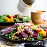 a white pitcher pouring dressing over a salad with beets and onions
