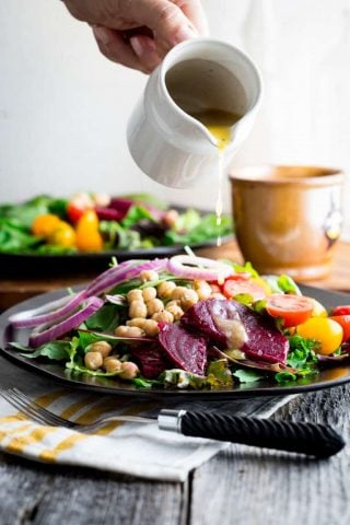 a white pitcher pouring dressing over a salad with beets and onions