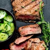 a flank steak on a slate board with sprigs of rosemary