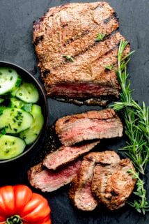 a flank steak on a slate board with sprigs of rosemary