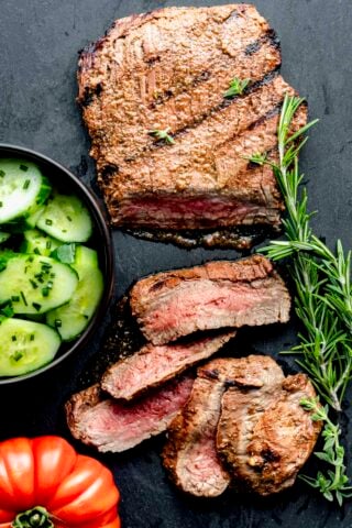 a flank steak on a slate board with sprigs of rosemary
