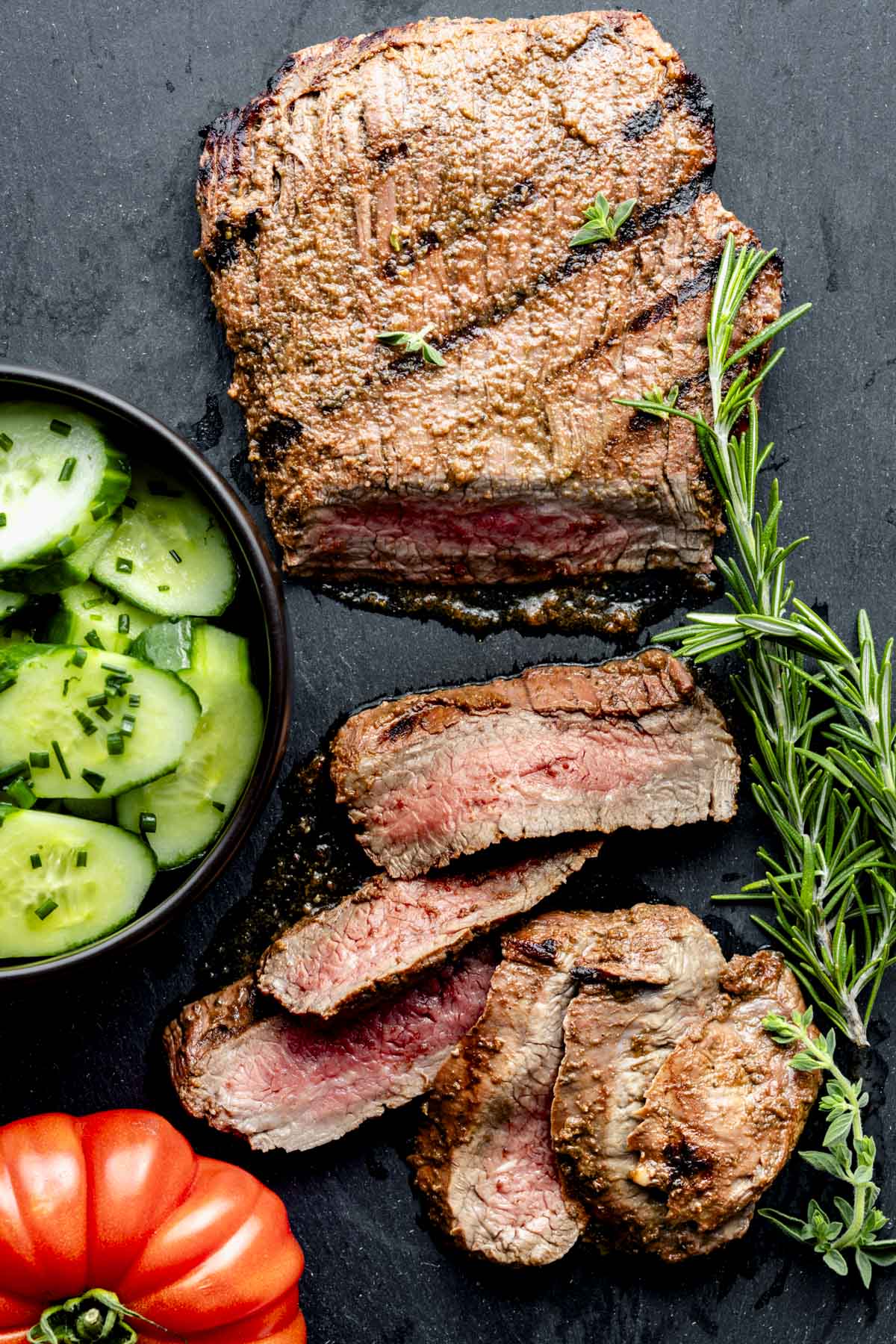 a flank steak on a slate board with sprigs of rosemary