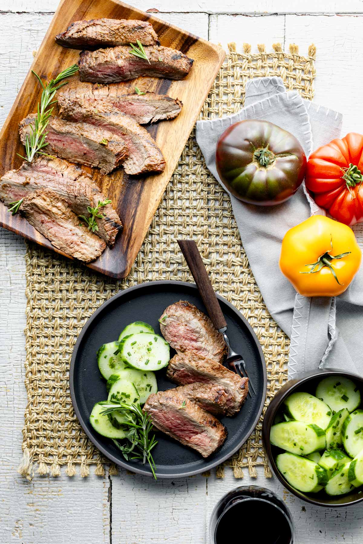 flatlay of the sliced steak, a plate of steak and cucumber salad and whole fresh tomatoes on the tabletop