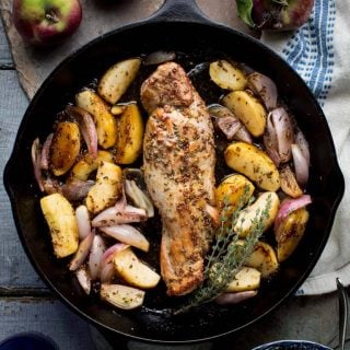 A cast iron skillet with pork tenderloin on a gray painted surface