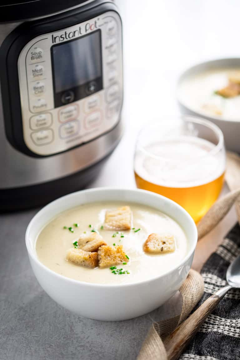 cauliflower soup in instant pot in a bowl alongside a glass of beer