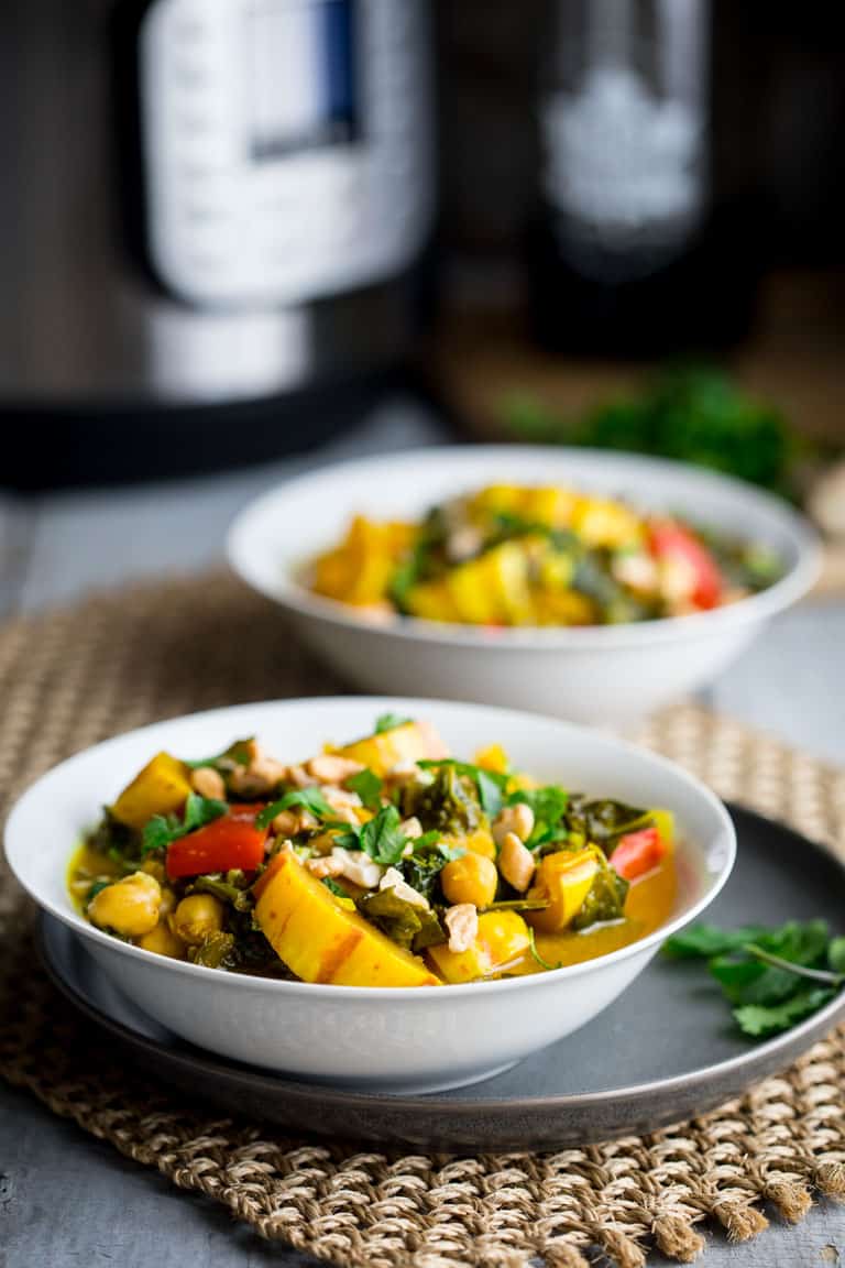 A view from the side of two white bowls on a woven mat with veggie curry in them, an instant pot is behind them