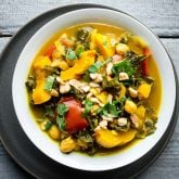 An overhead view of a white bowl filled with vegetable curry topped with cilantro and cashews on a gray painted surface