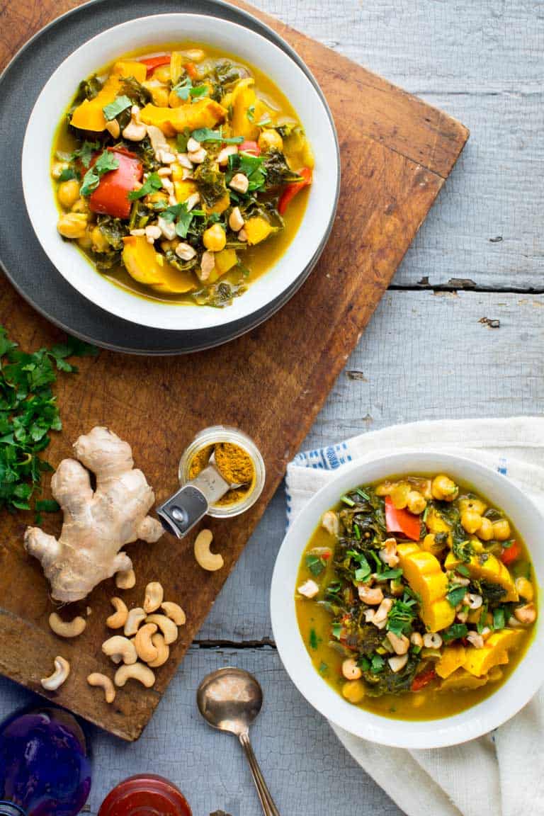 Instant Pot Veggie Curry in two bowls overhead with a cutting board with ginger, curry, cashews and cilantro on it.