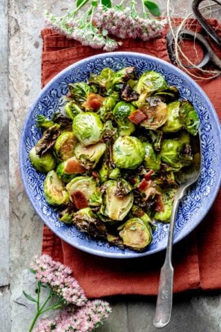 roasted brussels sprouts with crumbled bacon in a blue bowl on an orange napkin with sedum flowers