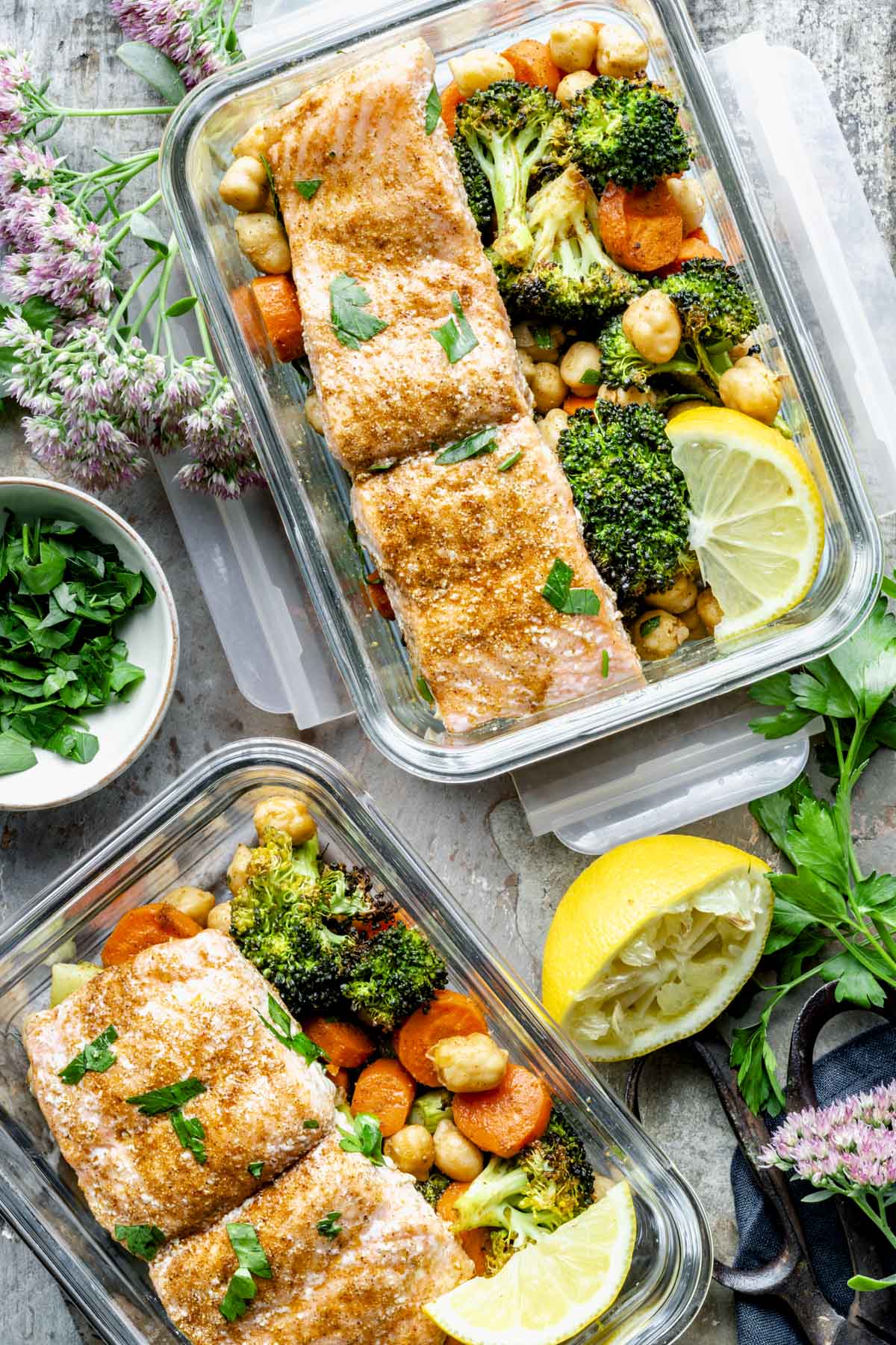 salmon packed into meal prep containers with veggies, chickpeas and lemon wedges.