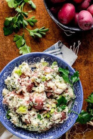 a blue bowl with rustic red-skinned mashed potatoes with herbs and a pot of red potatoes