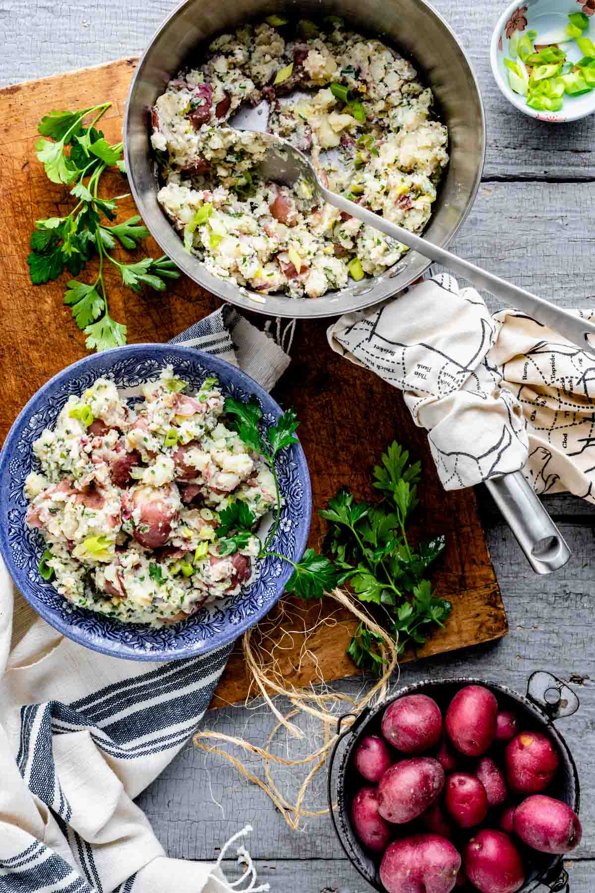 a pot of the potatoes plus the blue bowl of the mashed potatoes and a dish of whole red potatoes on a gray table