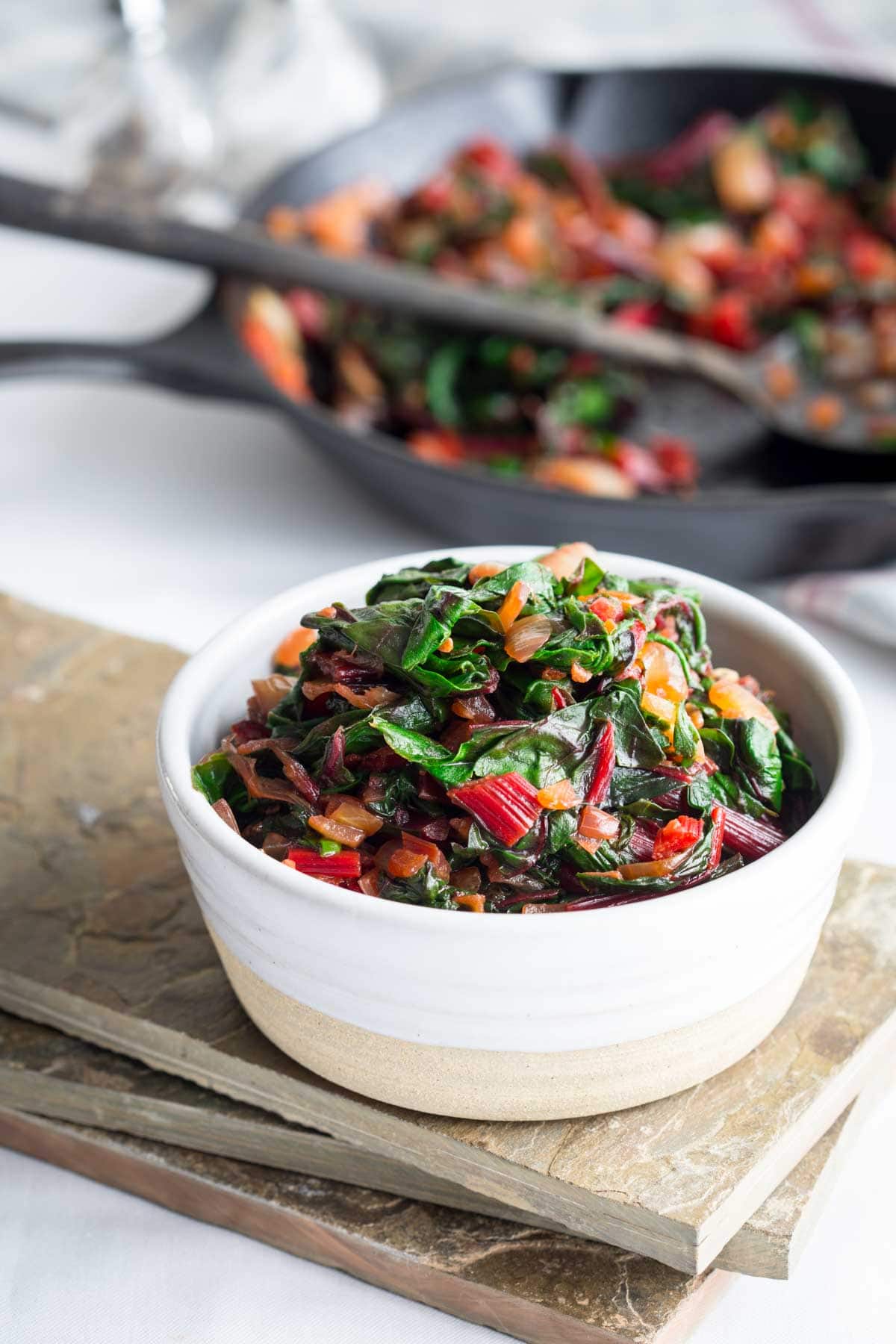 the chard in a white serving dish with the skillet in the background