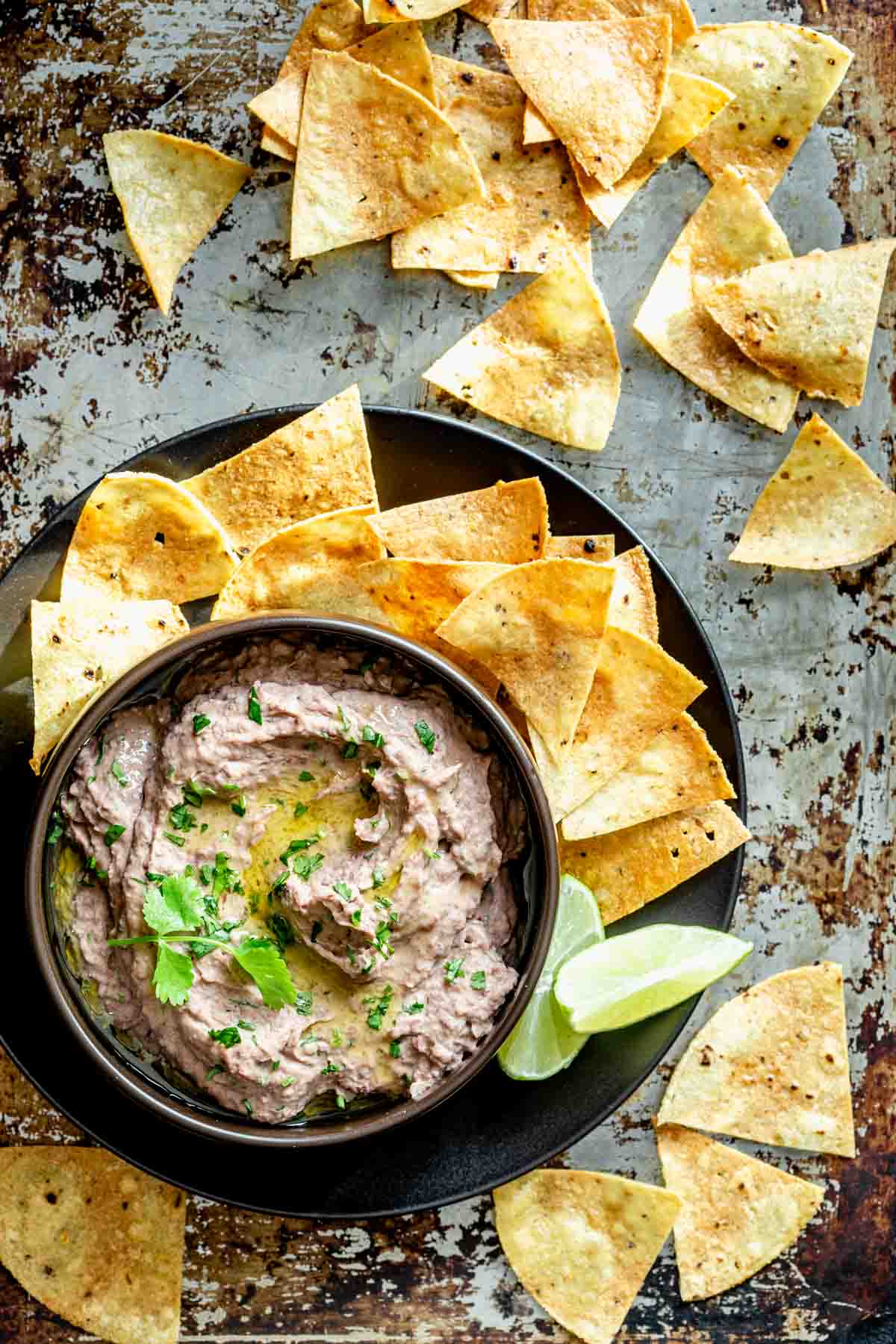 hummus and tortilla chips on a black platter with lime wedges on a metal sheet pan