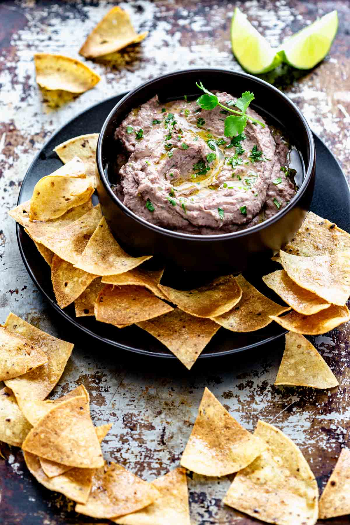 black bowl of black bean hummus with tortilla chips on a black platter